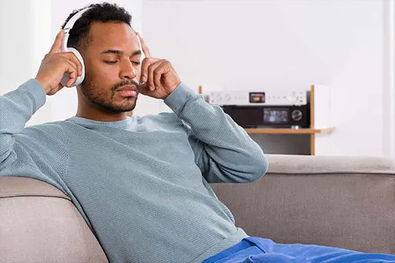 Person sitzt mit Over-Ear-Kopfhörer auf dem Sofa.