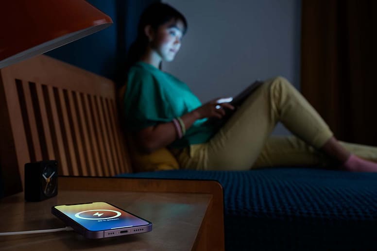 Handy liegt nachts auf einer induktiven Ladestation, Frau im Hintergrund sitzt auf dem Bett