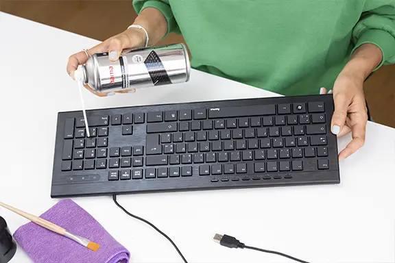 Person reinigt die Tastatur mit einem Gasdruck-Reiniger.