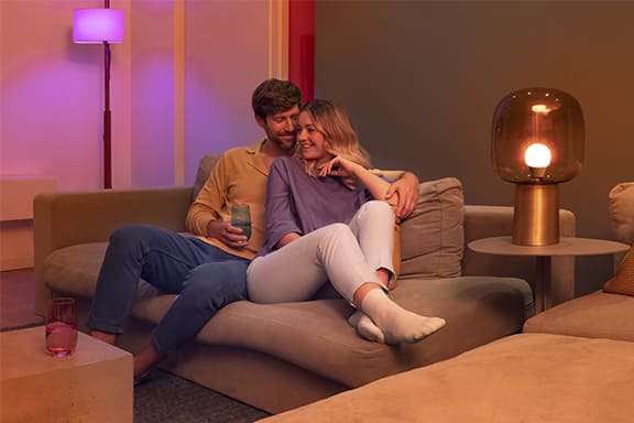 Zwei Personen sitzen auf der Couch in einem atmosphärisch beleuchteten Wohnzimmer.