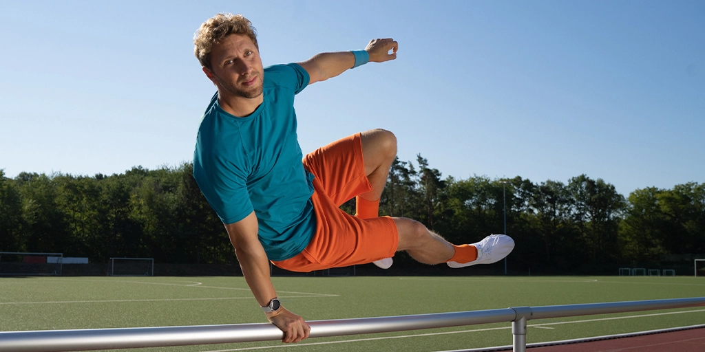 Sporttreibender Mann springt schwungvoll über Stange mit Smartwatch am Handgelenk