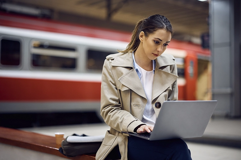 Eine Frau sitzt am Bahnsteig und arbeitet am Laptop