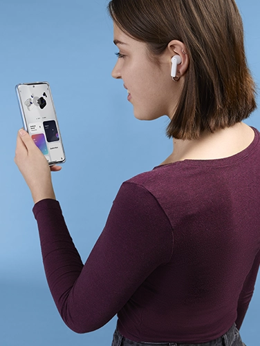 Junge Frau bedient ihr Smartphone und nimmt Einstellungen am Hama Bluetooth®-Kopfhörer "Passion Clear II" vor