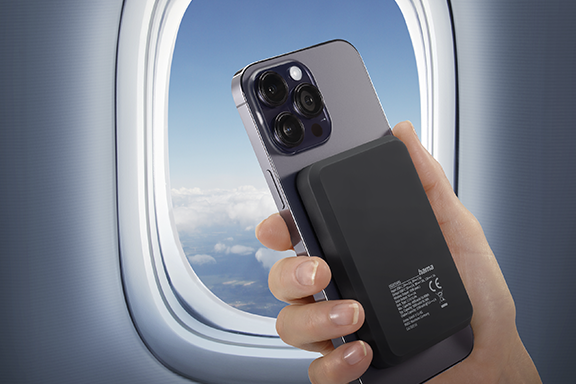 Person hält Smartphone mit wireless power pack vor einem Flugfenster im Flugzeug.
