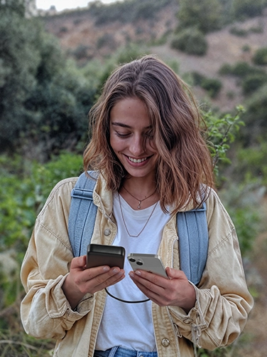 Eine junge Frau ist in der Natur wandern und bedient ihr Smartphone, während es mit dem Hama Power Pack "PD 20" geladen wird