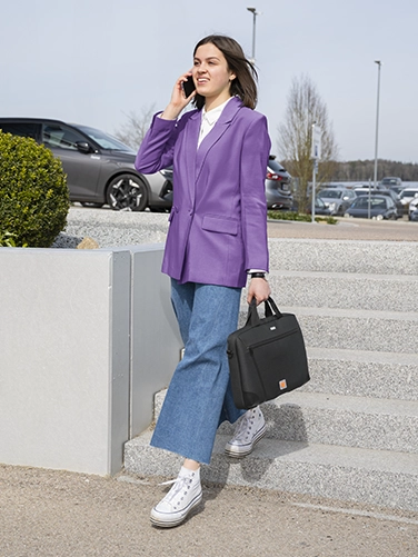 Eine junge Frau geht telefonierend eine Treppe im Außenbereich runter und trägt lässig die Hama Laptop-Tasche "Extreme Protect" in der Hand.