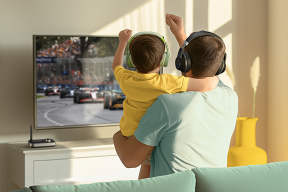 Vater und Sohn sitzen auf dem Sofa und bejubeln ein Formel1-Rennen - aber ganz leise, denn sie hören den Sound über Kopfhörer, die sie via Hama Bluetooth®-Adapter "Link.it duo" verbunden haben