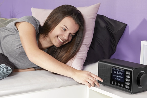 Junge Frau liegt im Bett und bedient ganz einfach das Hama Digitalradio "DR1000DE"