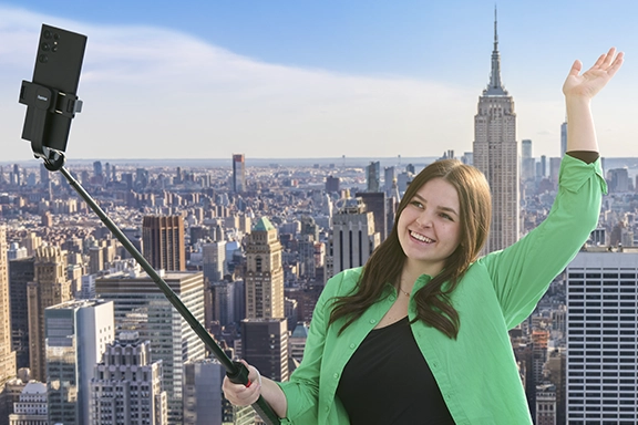 Eine junge Frau nimmt ein Selfie mit dem Hama Selfie-Stick-Stativ "Fancy Stand 170" vor der New Yorker Skyline auf